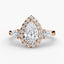 Rose gold three stone ring with a pear-shaped diamond and halo on a white background