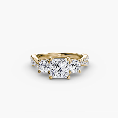 Three stone princess diamond ring with round side stone and u micro pave setting on twisted shank yellow gold on white background