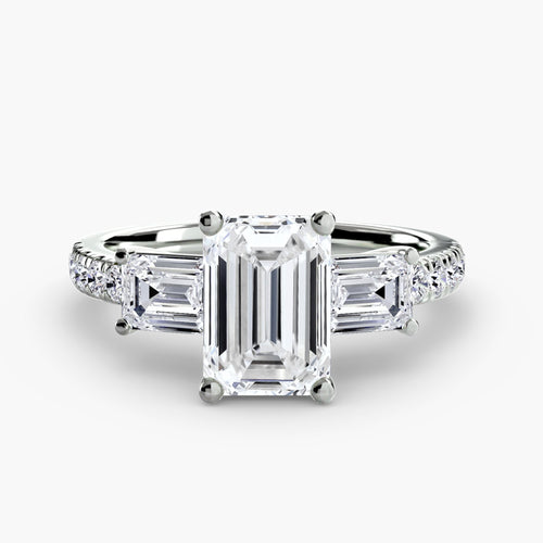 Three stone diamond ring with emerald-cut center stone and side stones u pave shank white gold on a white background