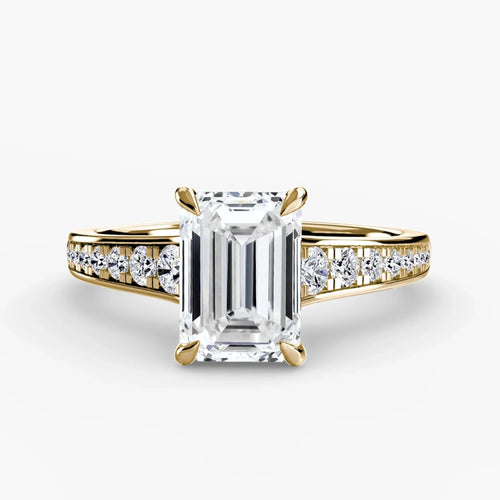 Gold ring with a large emerald cut diamond and smaller round diamonds on the band against a white background
