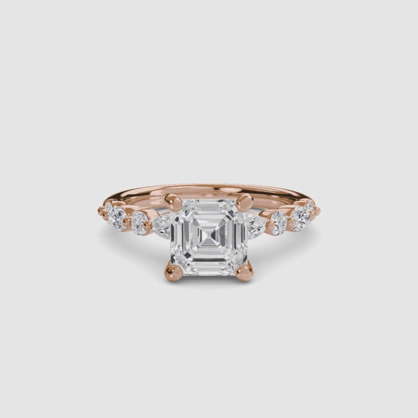 Rose gold ring with a large Asscher-cut diamond and smaller diamonds on the band marquise and round on a white background