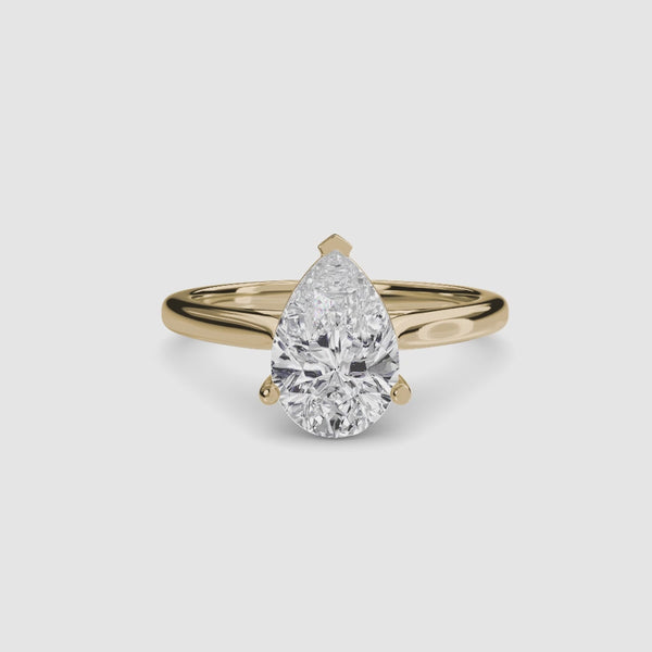 Solitaire gold ring with a pear-shaped diamond on a white background
