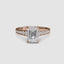 Rose gold ring with a large emerald cut diamond and smaller round diamonds on the band against a white background