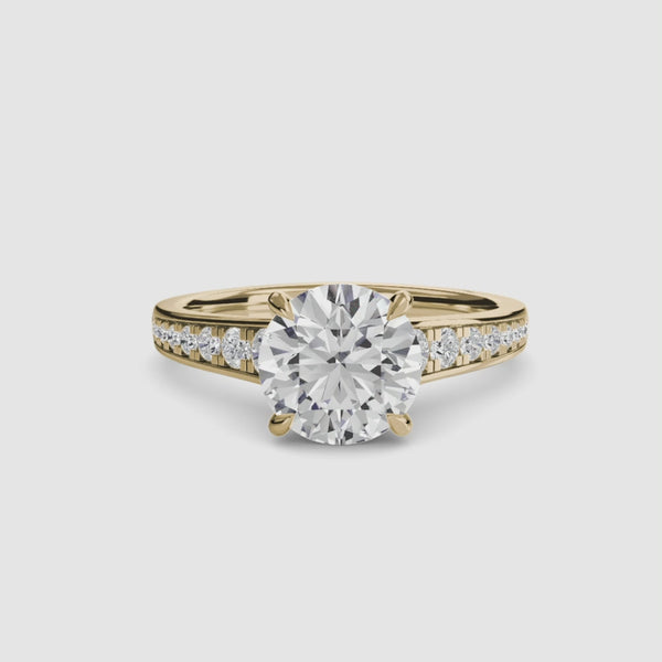 Gold ring with a large round diamond and smaller diamonds on the band against a white background