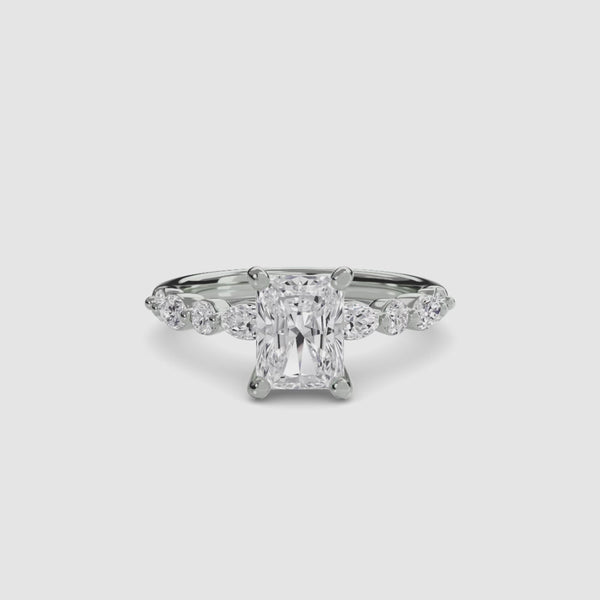 White gold ring with a central radiant cut diamond and marquise and round side stones on the band on a white background