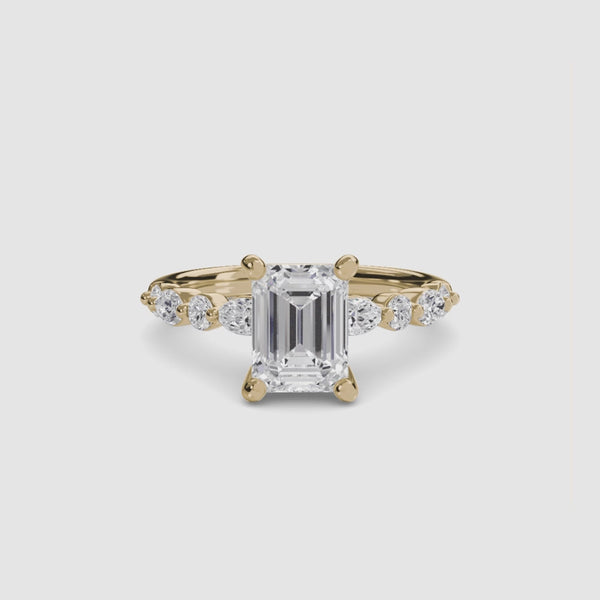 Gold ring with a large emerald-cut diamond and smaller diamonds on the sides against a white background