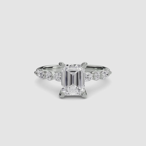 White gold ring with a large emerald-cut diamond and smaller diamonds on the sides against a white background