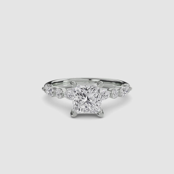 Gold ring with a large central princess diamond and smaller diamonds on the band against a white background