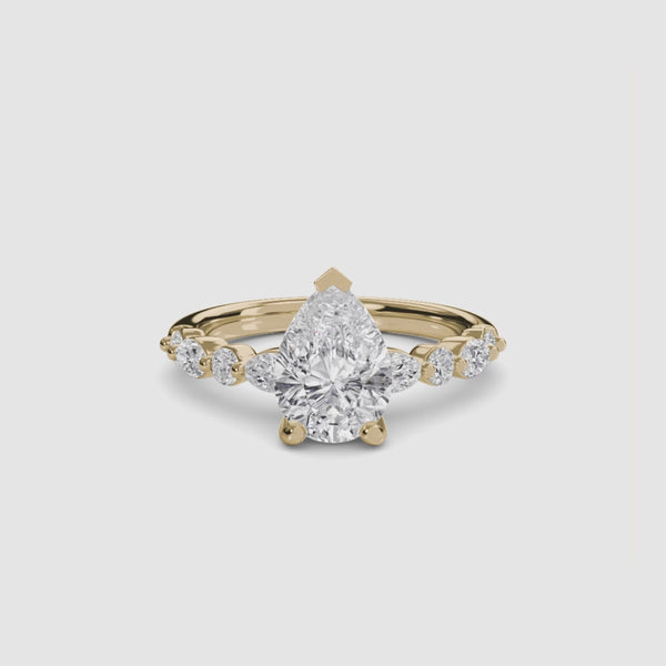 Pear shaped diamond ring with marquise and round side stones yellow gold on a white background