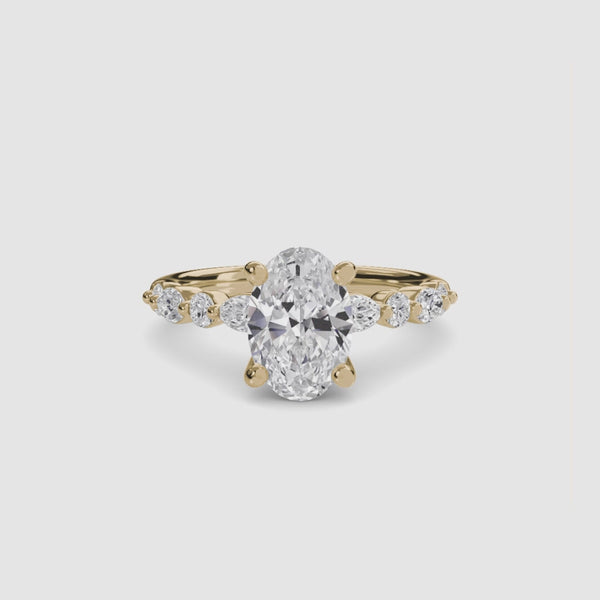 Gold ring with a large oval cut diamond and smaller marquise round diamonds on the sides of the band against a white background