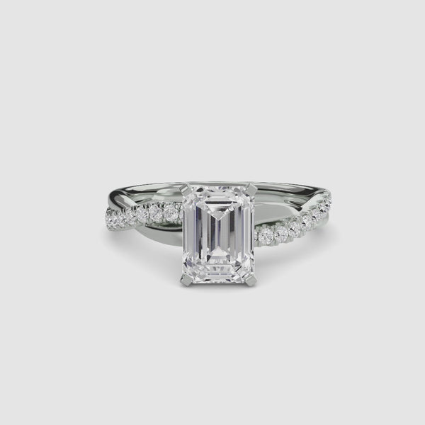 White gold ring with a large emerald-cut diamond and smaller diamonds on the twisted band against a white background