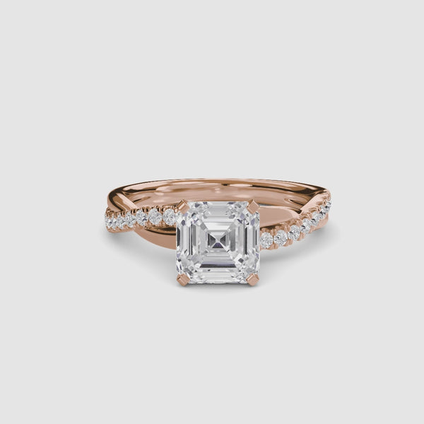 Rose Gold ring with a large Asscher diamond and smaller diamonds on the twisted band against a white background