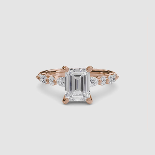 Rose gold ring with a large emerald-cut diamond and smaller diamonds on the sides against a white background