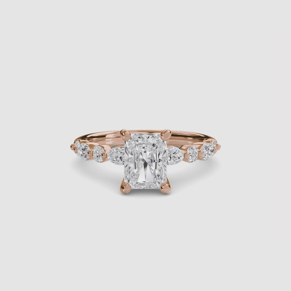 Rose gold ring with a central radiant cut diamond and marquise and round side stones on the band on a white background