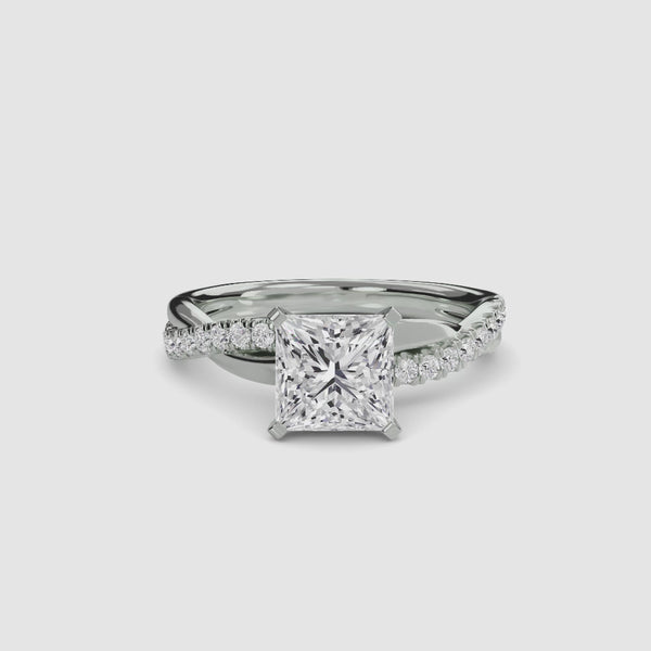 White gold ring with a large princess-cut diamond and smaller diamonds on the twisted u-pave band against a white background