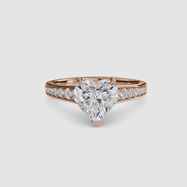 Heart-shaped diamond ring with rose gold round diamonds pave band on a white background
