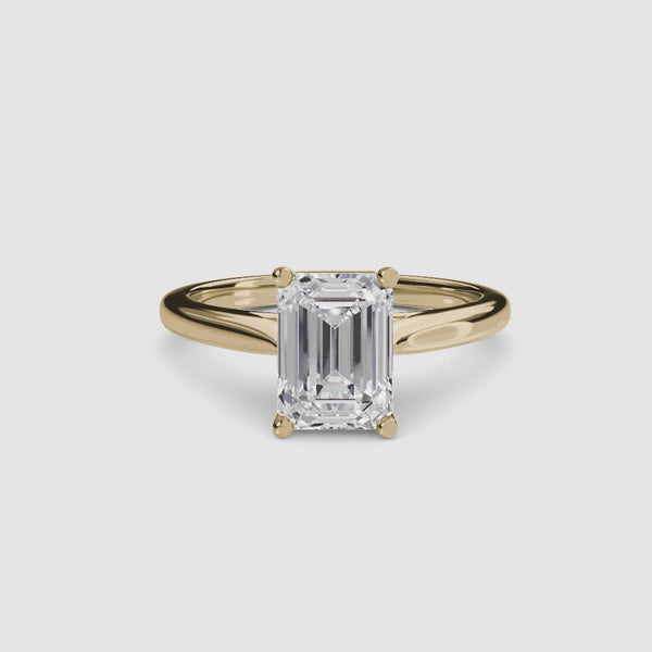 Solitaire gold ring with a large emerald-cut diamond on a white background