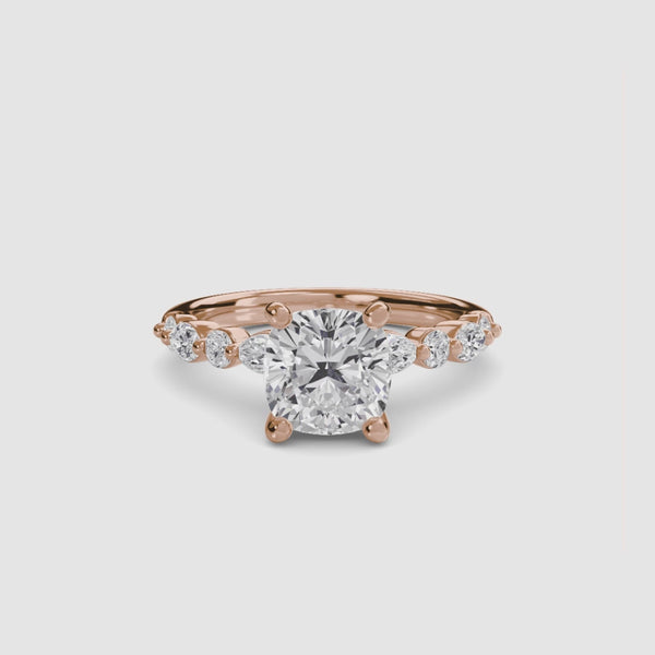 Gold ring with a large cushion cut diamond and smaller marquise shaped and round cut diamonds on the band against a white background